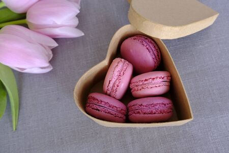 Heart shaped gift box with sweet french macarons, pink spring flowers on grey background. Almond meringue based sandwich cookies, fruity flavours.の写真素材