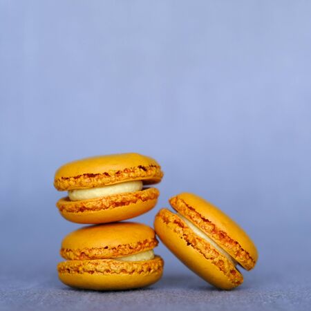 Stack of fresh tasty orange macarons sandwich cookies on gray background, close up. Copy space. French confectionery.の写真素材