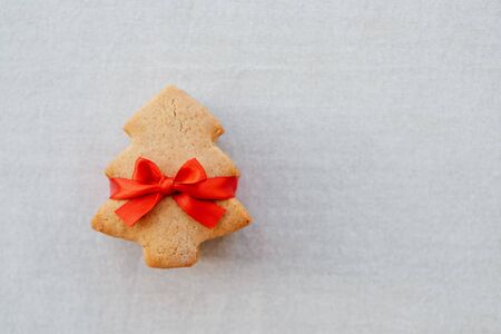 Stack of shortbread cookies in the shape of Christmas tree with beautiful festive red ribbon on light tablecloth background. Copy space. Flat lay, top view. Sweet homemade gift. New year postcard.の写真素材
