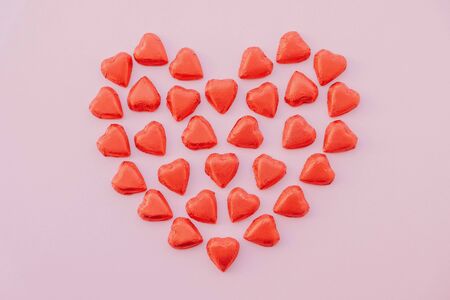 Heart shape made of red sweet chocolates on pastel pink background. Flat lay, top view. Love concept. Valentine's Day, Mother's day, Birthday card.の写真素材
