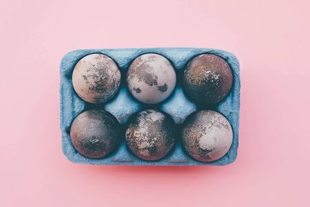 Natural dyed gray colored eggs in blue egg box on pastel pink background, top view. Flat lay. Happy Easter. Copy space.の写真素材