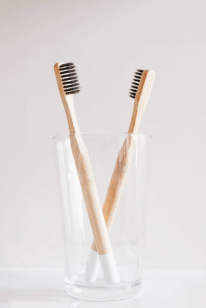 Stylish eco friendly natural bamboo toothbrushes in a glass against white background in bathroom.