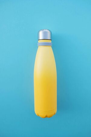 Stylish reusable eco-friendly thermo stainless steel yellow bottle on light blue background. Space for text. Zero waste, plastic free and sustainable lifestyle concept. Top view, flat lay.の写真素材