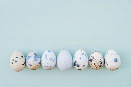 Happy Easter. Beautiful colorful quail eggs on pastel light blue background, close up, top view....