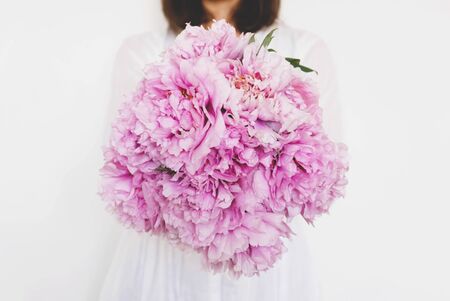 Woman holding beautiful bunch of fresh pink peony flowers in full bloom against white background, close-up. Blooming peonies. Copy space. Mother's day.の写真素材