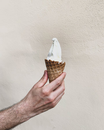 Hand holding delicious refreshing ice cream cone against pastel beige background. Copy space. Summer...