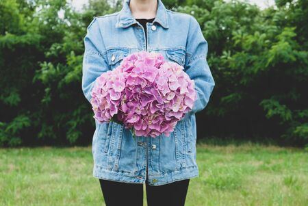 Millennial girl wearing denim jacket holding big bunch of fresh purple hydrangea flowers in full bloom, close up. Copy space. Summer bouquet.の写真素材