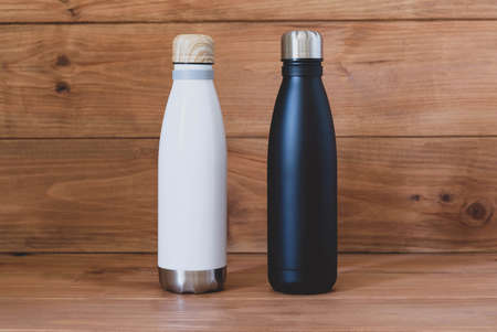 Reusable eco-friendly black and white stainless steel thermo bottles on wooden rustic background. Copy space. Zero waste, no plastic, sustainability. Bring your own water bottle concept.の写真素材