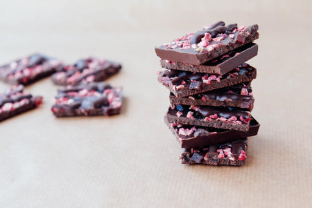 Pieces of dark chocolate with red fruits stacked on baking paper background.