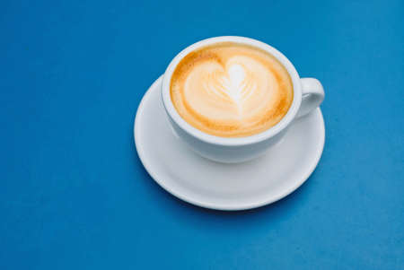 Cappuccino coffee in white cup with latte art on blue background.の写真素材
