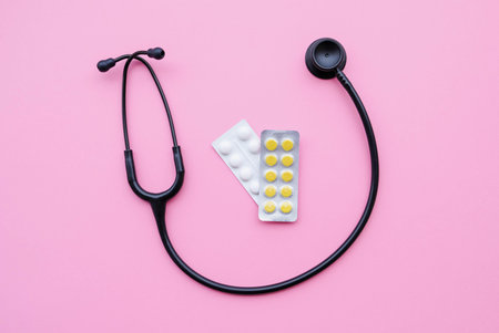 Black modern stethoscope and tablets on pink background.