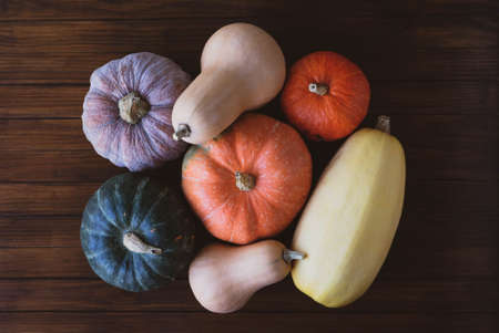 Different types of colorful pumpkins on dark wooden rustic background, top view, close up. Halloween or Thanksgiving holiday preparations. Fall harvest.の写真素材