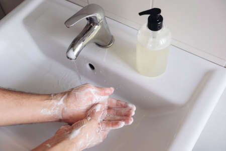 Washing hands concept. Man cleaning his hands using liquid disinfectant soap and water in bathroom, close up. Personal hygiene, health care and coronavirus prevention.の写真素材