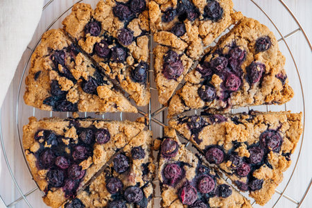 Freshly baked oat blueberry scones on cooling rack on white wooden background. Sweet food with...