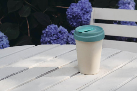 Reusable eco-friendly bamboo cup with lid on white wooden garden table.