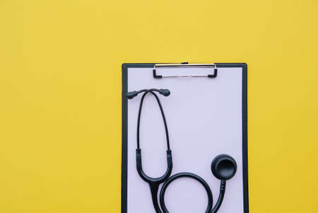 Black stethoscope and blank medical form on yellow background.の写真素材
