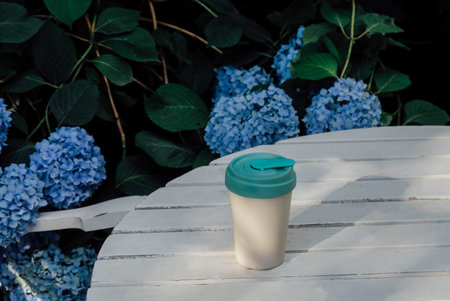 Reusable eco-friendly bamboo cup with lid on white wooden garden table.
