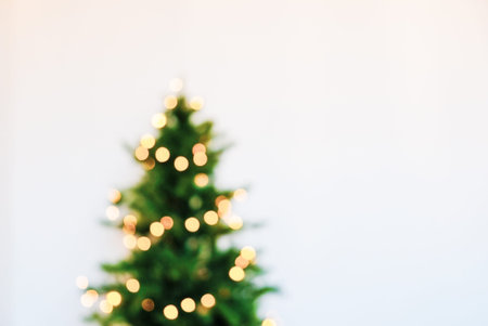 Blurred fir tree with yellow festive lights against white background.