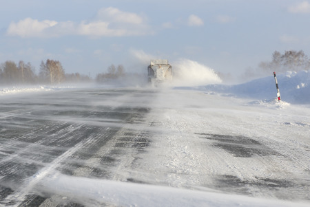 Emergency road service track cleans road after strong winter blizzard with snowdrift on the highwayの写真素材