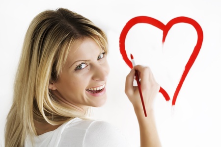 wsmiling young woman drawing heart-shape on white wallの写真素材