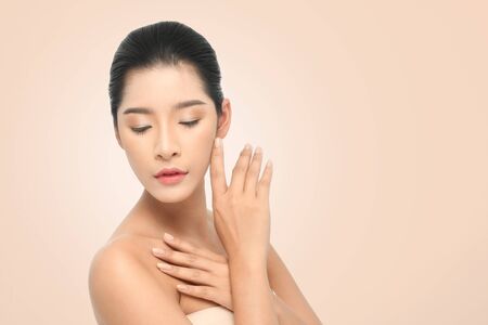 Beautiful Young Woman with clean fresh skin, Proposing a product. Gestures for advertisement on beige backgroundの写真素材