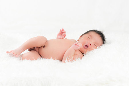 Newborn infant boy is sleeping peacefully while snuggled in the bed with a white cloth.