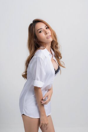 Beautiful asian woman wearing a white shirt in a sitting position on isolated gray background.の写真素材