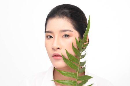 Beautiful asian young woman with clean fresh skin holding green plant on white background.の写真素材