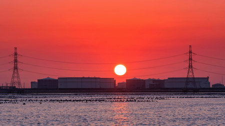 Oil storage tank at oil terminal is industrial facility is located by the sea at sunset on big sun...