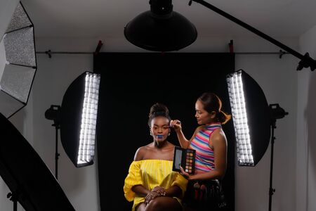 Professional make up artist working with african fashion model at photo studio with many equipment for photography. Light modifier, flash, Beauty Dish, Stripbox, Reflector.の写真素材