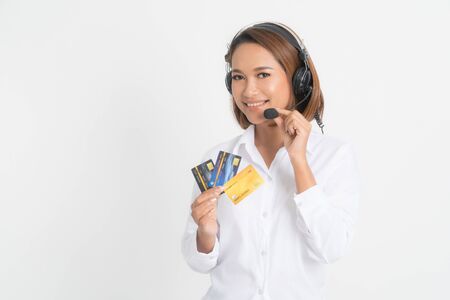 Friendly female helpline operator or call center showing blank credit card, headset holding her arms crossed isolated on white background.の写真素材