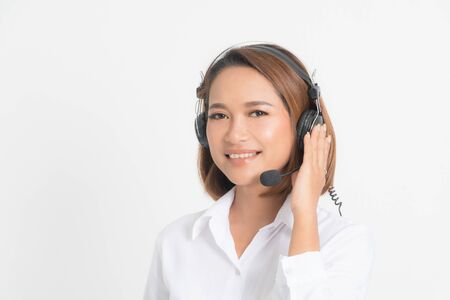 Portrait of happy smiling female customer support phone operator short hair, wearing a white shirt with headset standing one side holding the earphone isolated on white background.の写真素材