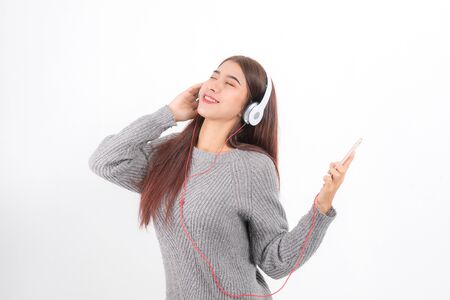 Young beautiful woman wearing a gray sweater is lying and listening to music wearing white music headphones isolated on white background. She is relaxing and happinessの写真素材