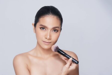 Beautiful Young Woman with clean fresh skin, Proposing a product with Makeup brush Gestures for advertisement on white backgroundの写真素材