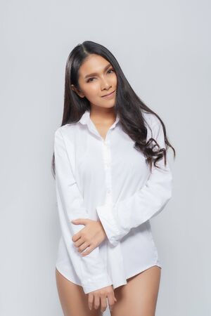 Beautiful asian woman wearing a white shirt in a sitting position on isolated gray background.の写真素材