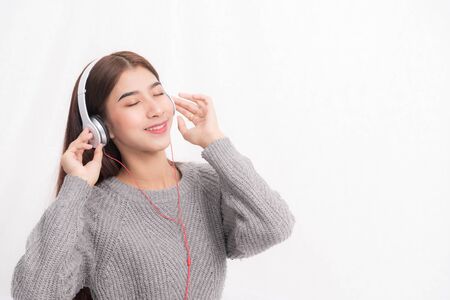Young beautiful woman wearing a gray sweater is lying and listening to music wearing white music headphones on white wall background. She is relaxing and down with eyes closed at happiness.の写真素材