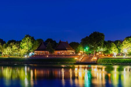 Beautiful thai traditional house style in ancient thai way is located by the river during the night time which lights up beautifully.の写真素材