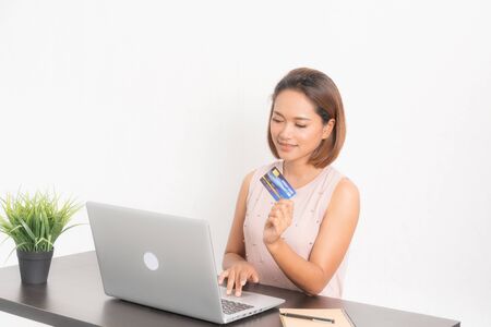 Young woman entrepreneur using credit card and laptop for paying online, She is sitting on white background.の写真素材