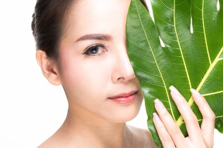 Close-up studio shot, Beautiful young woman with clean fresh skin holding green leaves. Proposing a product. Gestures for advertisement isolated on white background.の写真素材