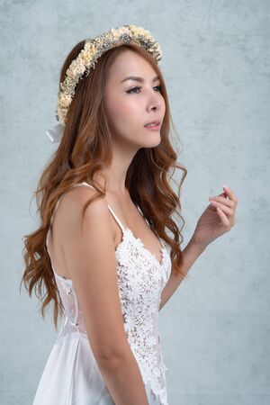Vintage style portrait beautiful woman wearing a white dress, flower crown on gray soft blurred background.の写真素材
