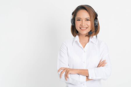 Call center operator woman short hair, wearing a white shirt with headset standing crossing her arms isolated on white background.の写真素材