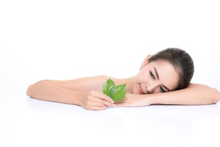 Close-up studio shot, Beautiful young woman with clean fresh skin holding green leaves. Proposing a product. Gestures for advertisement isolated on white background.の写真素材