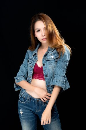 Beautiful asian woman long brown hair fashion sexy portrait wears red underwear, jeans and jacket jeans on black background.の写真素材