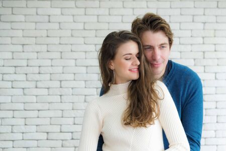 European couples, caucasian man wearing blue sweater and woman wearing white sweater, are standing happily hugging each other in the room.の写真素材