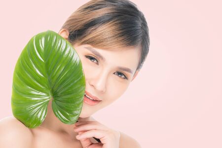 Close-up studio shot, Beautiful young woman with clean fresh skin holding green leaves. Proposing a product. Gestures for advertisement isolated on white background.の写真素材