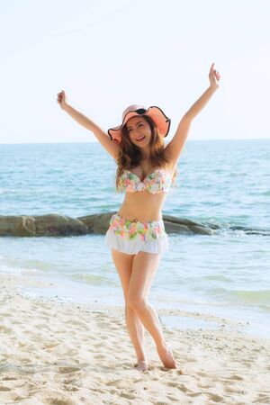 Portrait beautiful young woman wearing summer hat with brim, She is smiling and happiness jumping on the beach.の写真素材