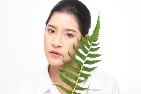 Close-up studio shot, Beautiful young woman with clean fresh skin holding green leaves. Proposing a product. Gestures for advertisement isolated on white background.の写真素材