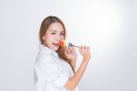 Asian woman portrait with perfect skin smiling face happy, wearing white dress, holding a bowl of vegetable salad and fork on white background.の写真素材