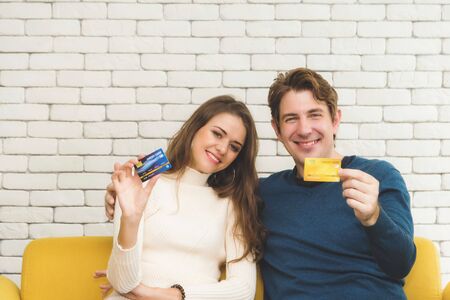 European couples, caucasian man wearing blue sweater and woman wearing white sweater, are showing two credit card in their hand in happiness. concept of spending couple.の写真素材