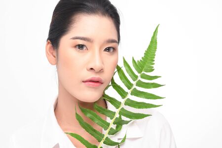 Close-up studio shot, Beautiful young woman with clean fresh skin holding green leaves. Proposing a product. Gestures for advertisement isolated on white background.の写真素材